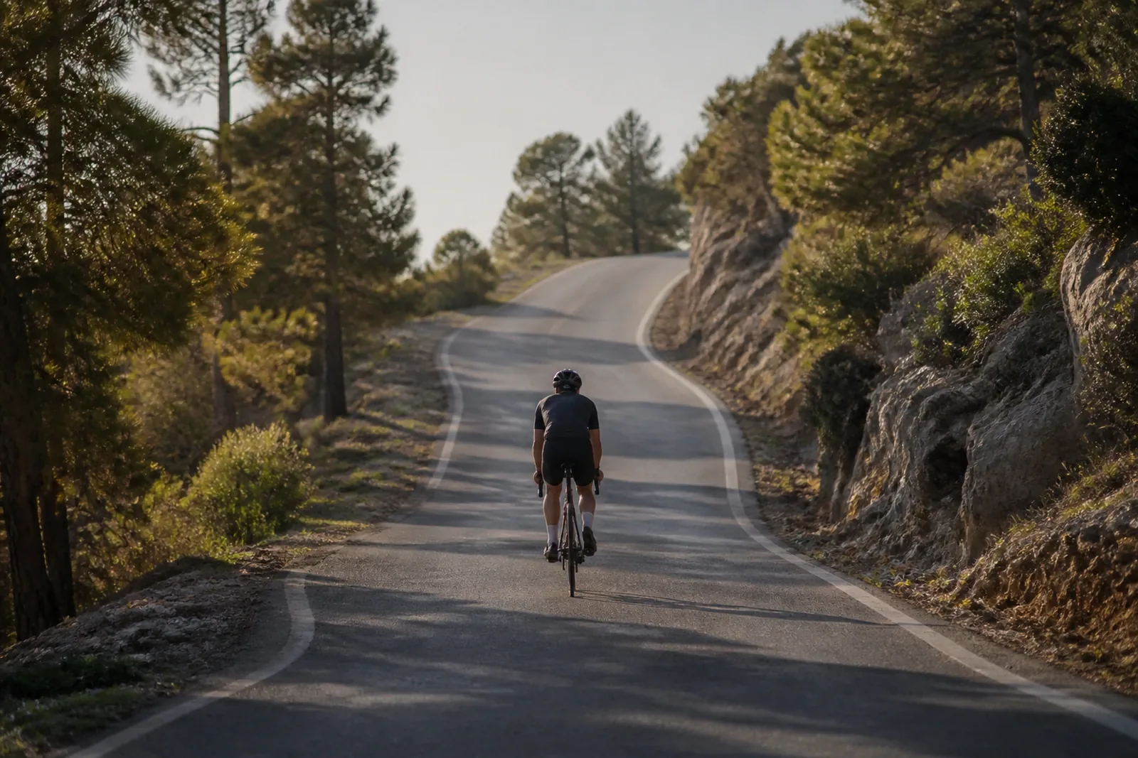 Lone cyclist climbing an empty, winding mountain road